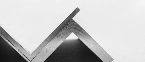 Metalowy kątownik stalowy o wymiarach 90 mm x 60 mm x 8 mm ułożony na ciemnym tle