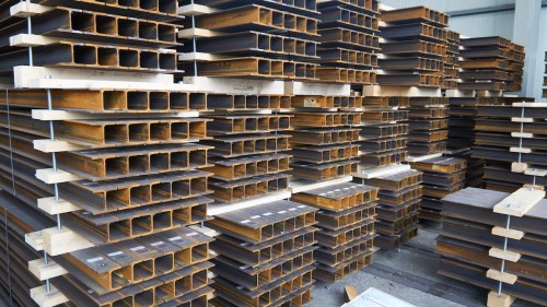 Stalowe dwuteowniki HEM ułożone w stosy na drewnianych paletach w magazynie przemysłowym