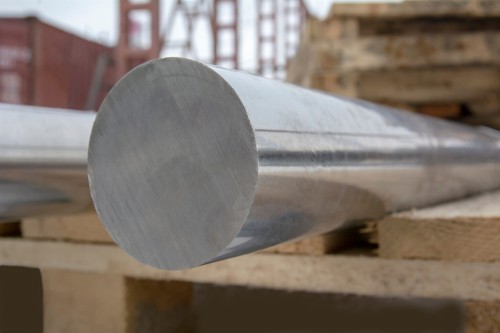 Pręt okrągły nierdzewny o średnicy 12 mm leży na drewnianej palecie w tle konstrukcja metalowa